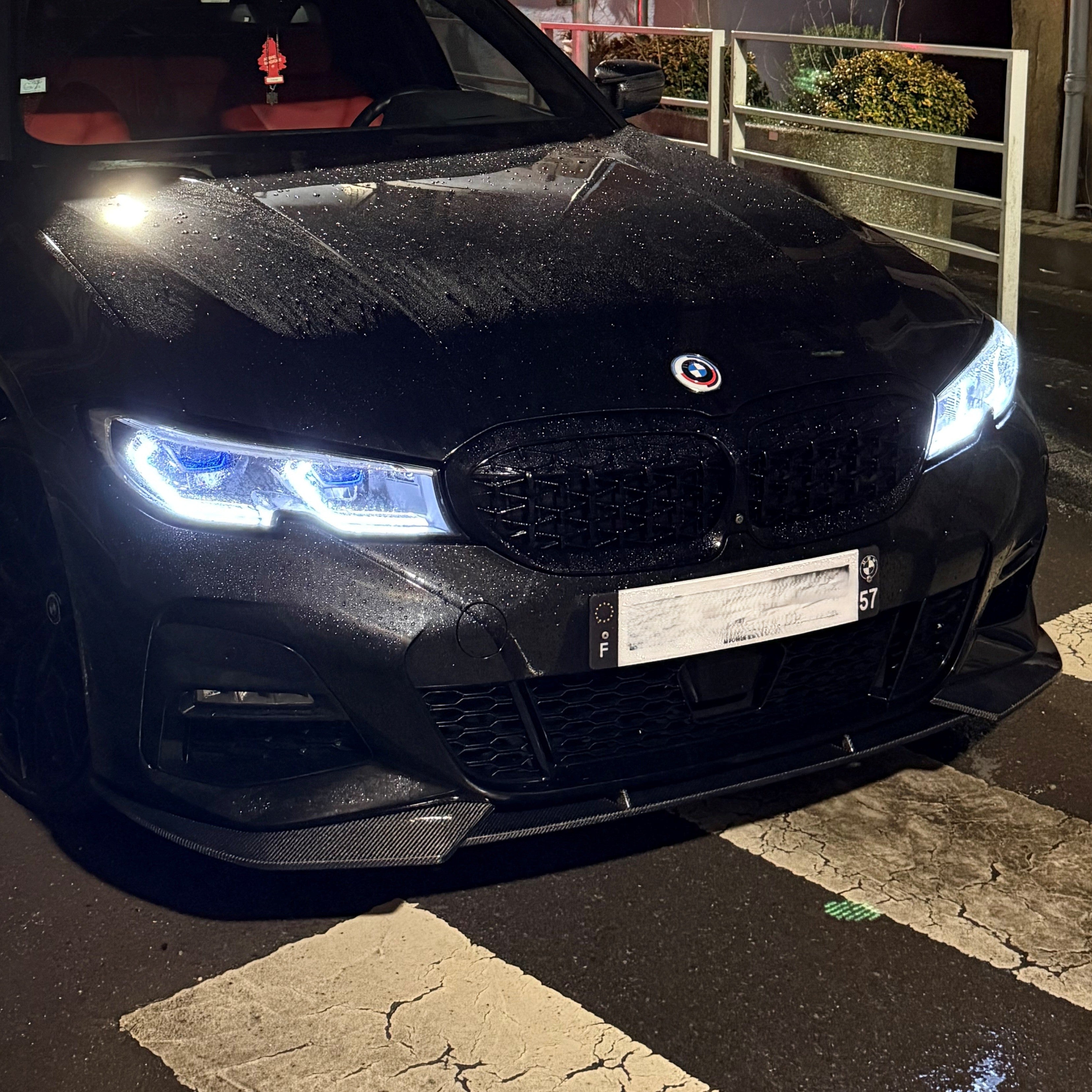 Front view of a black car with illuminated headlights on a street at night.