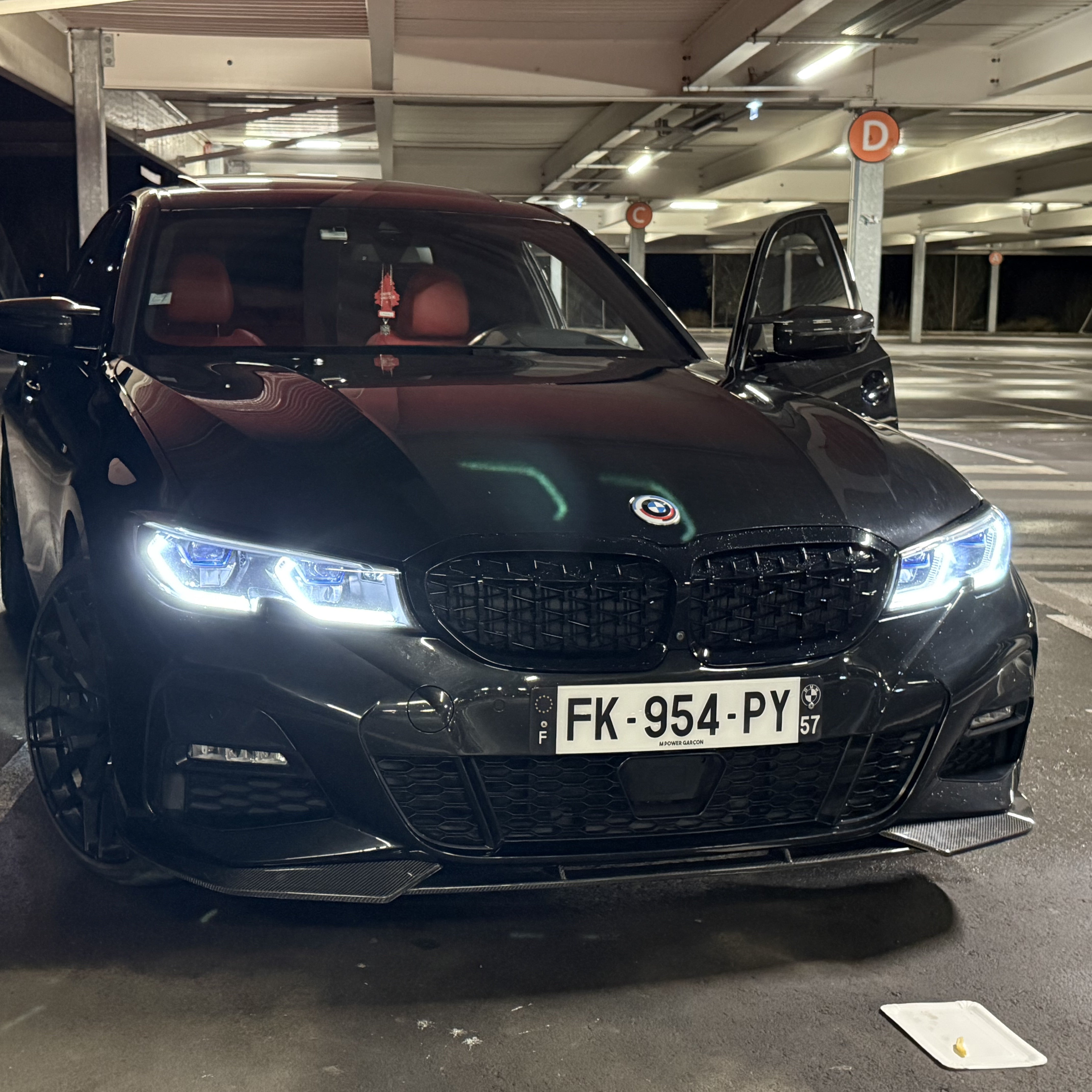 Black BMW car in a parking garage with illuminated headlights.