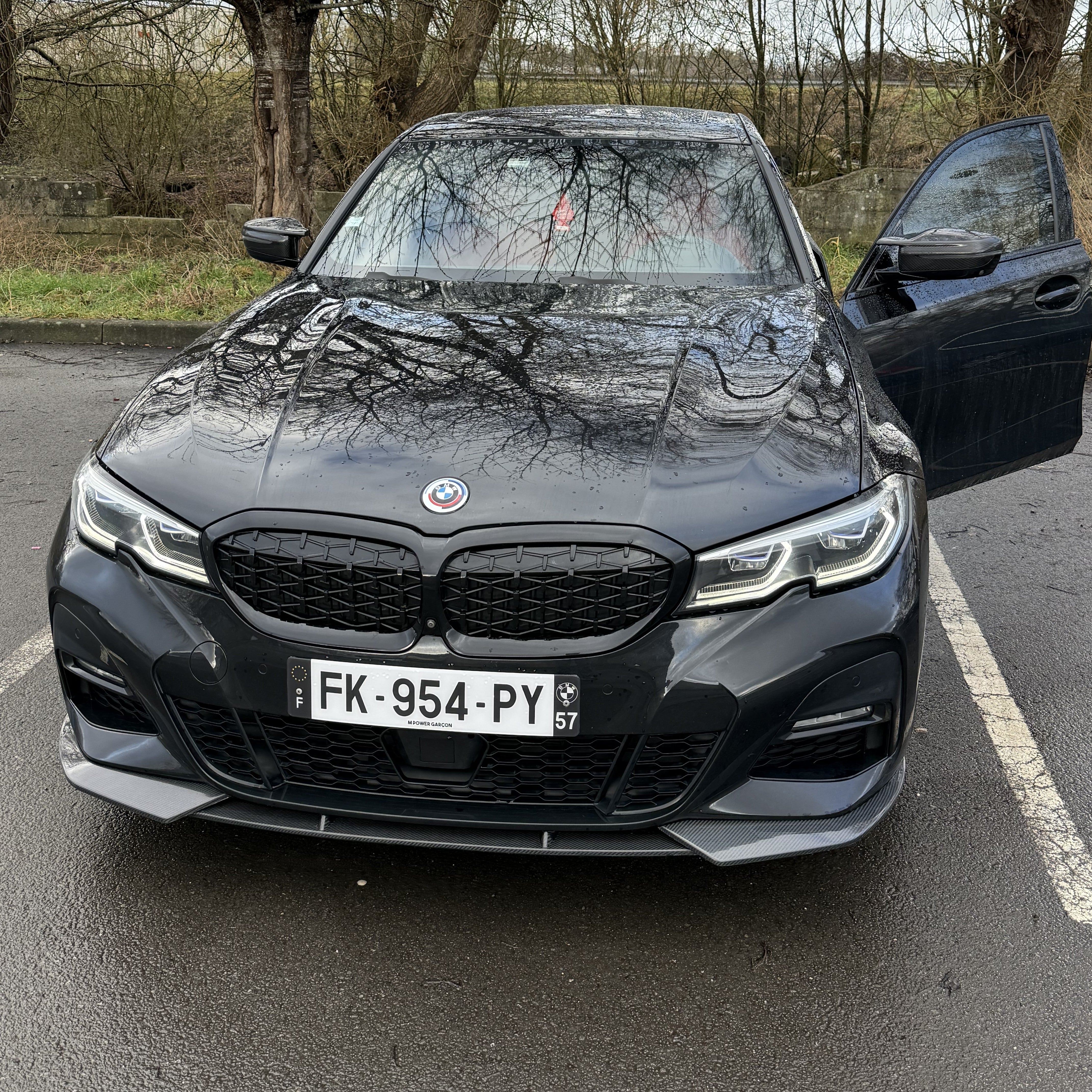 Black BMW car with open door on a road with trees in the background